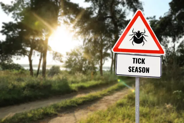 a hudson county nj park during spring featuring a warning sign that reads "tick season"